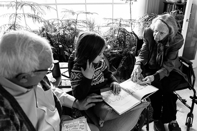 Young boys sits between grandpa and great-grandmother reading a book.