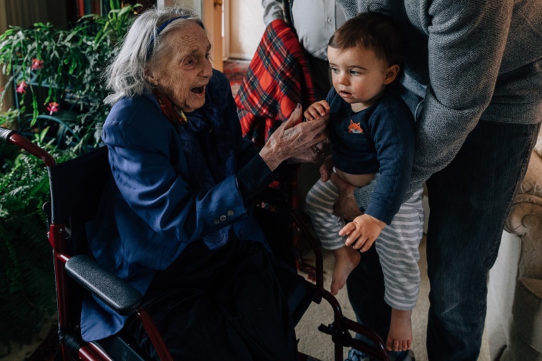 Infant boy looks at great-grandmother as she anticipates holding him. 