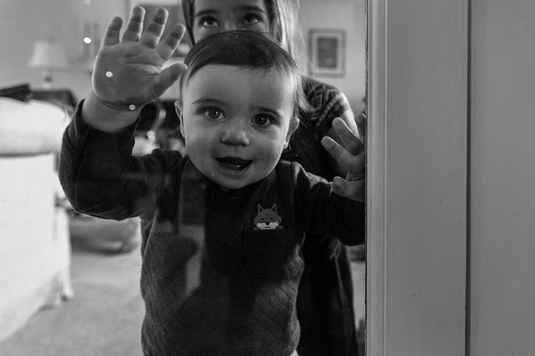 Baby smiles through a glass door with a mixture of reflection and transparency.