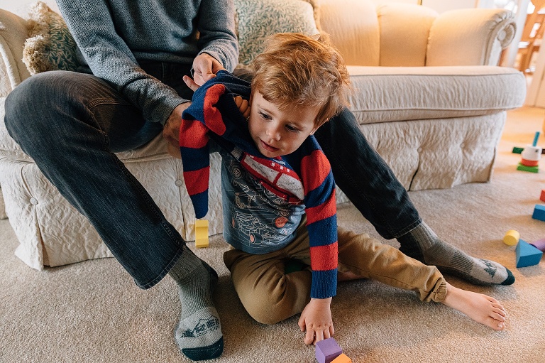 Dad helps son put a sweater on. Their body language is the same.