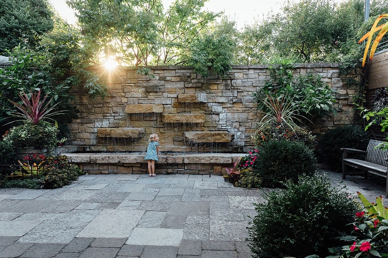 young girl explores a fountain at Olbrich Gardens at the sun is setting and coming over the top of a brick wall