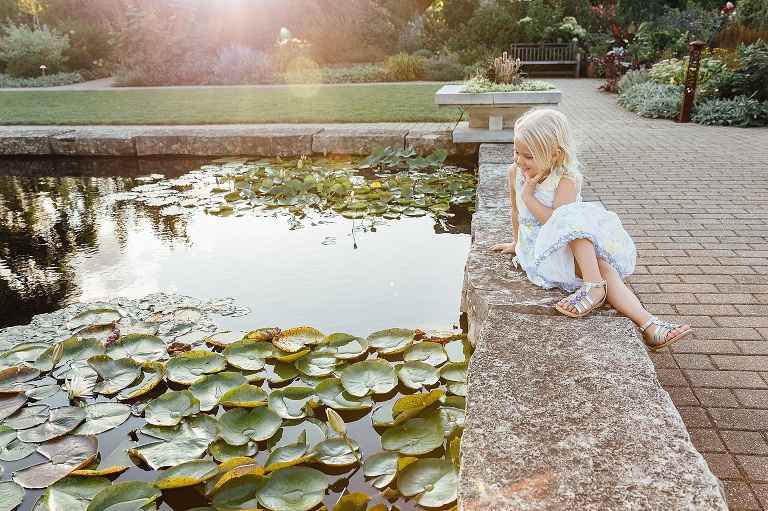 Young girl sits on the edge of a reflecting pond with warm sunflare coming in on top of image. Olbrich Gardens