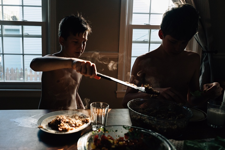 Boy uses tongs to grab hot foot out of a bowl at the dining room table. Steam is visible.