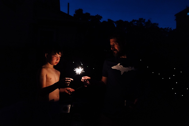 Man and young boy light a sparkler at dusk