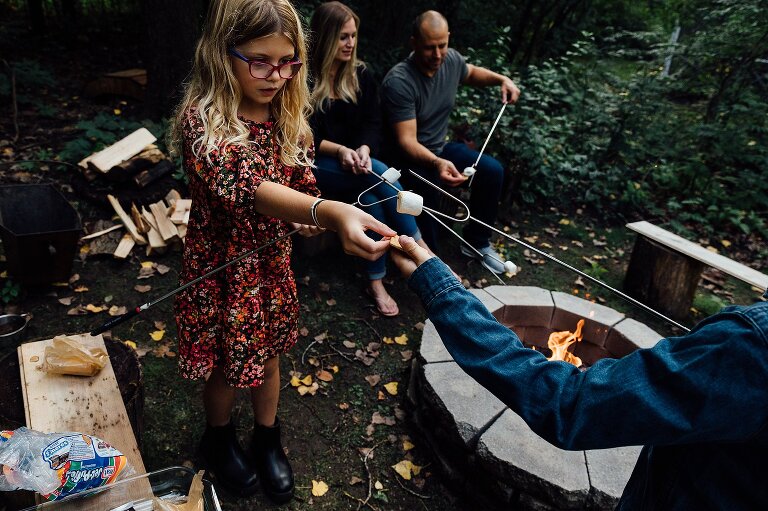 Family of 4 reaching and assembling s'mores next to fire pit
