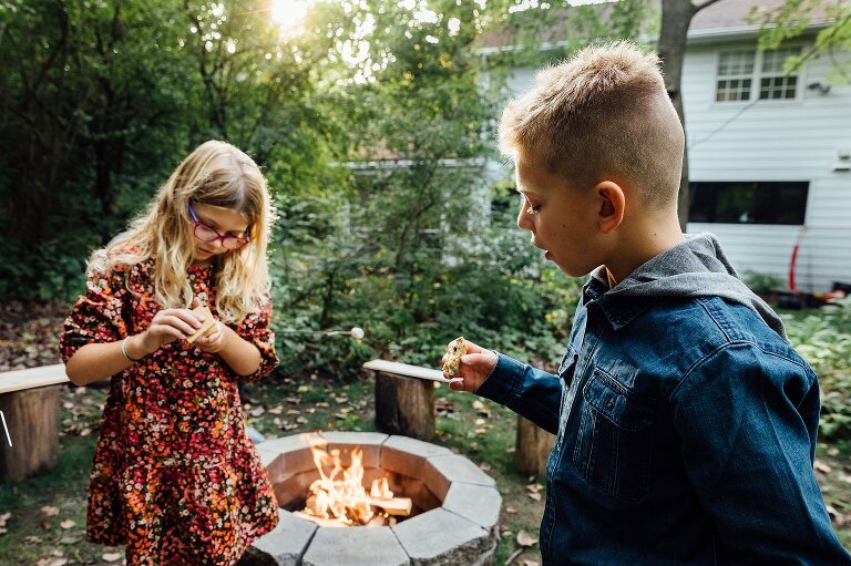 A boy and a girl assemble s'mores next to a fire pit