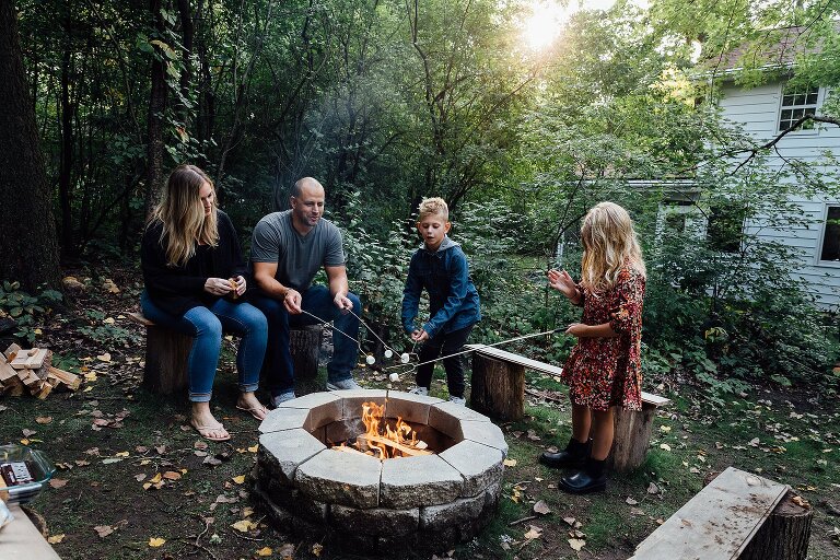 family of four roast marshmallows over circular fire pit in their backyard 