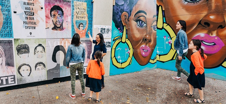 mom and two girls walk in front of colorful murals in downtown Madison. 