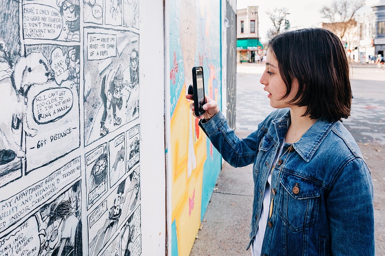 girl takes picture on her phone of murals in downtown Madison