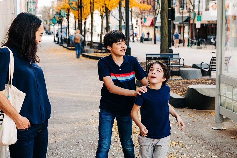 Teen boy smiles as he holds his little brother's shoulders as brother looks upward