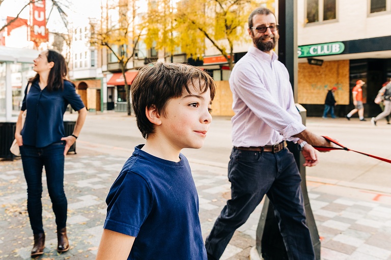 Boy smiles looking off camera, dad smiles at boy, mom in background smiling off camera.  Bright yellow trees in background 