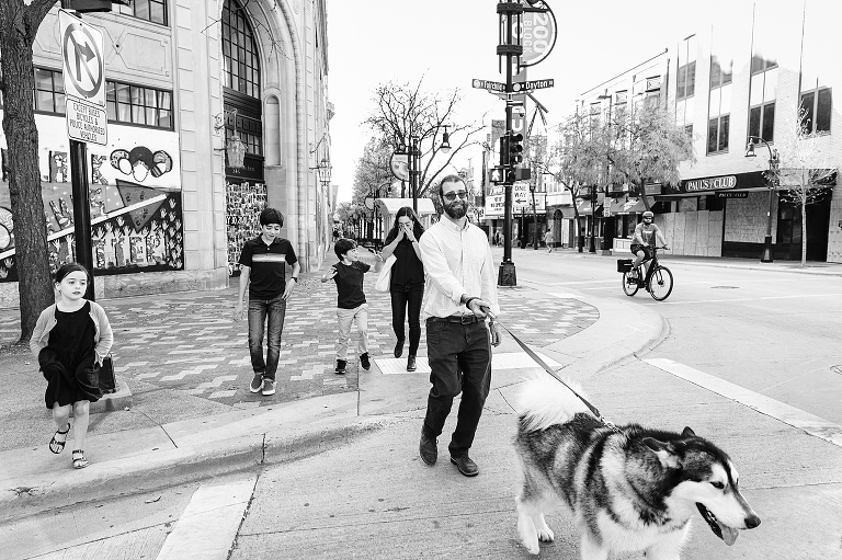 black and white. Mom wipes away tears while rest of family crosses busy urban street in downtown Madison