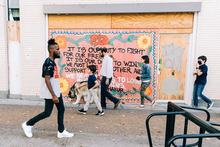 family and dog walk in front of mural in downtown Madison, pedestrian walks in opposite direction 
