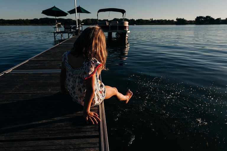 Girl on a dock dangles her feet in the lake
