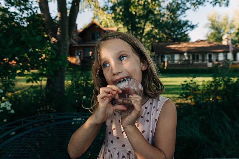 Girl licks bowl clean in backyard. 