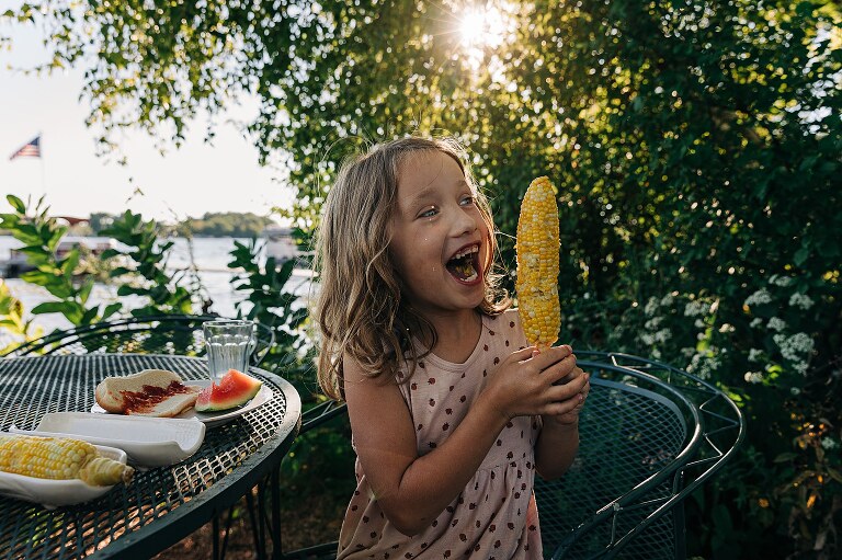 Girl laughs while eating corn. 