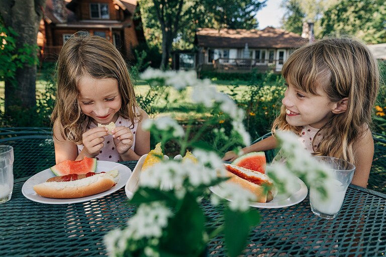 Two girls eat at metal table outdoors. 