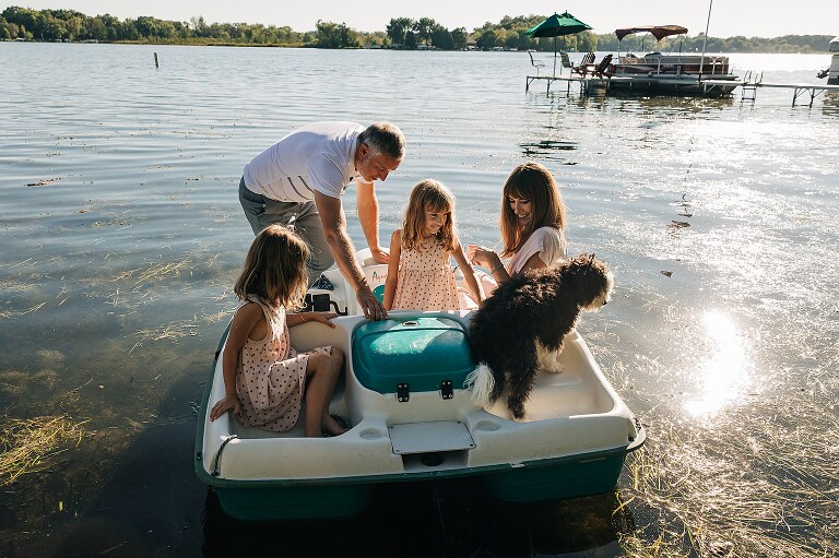Family of four and their dog ride on a paddle boat in the lake 
