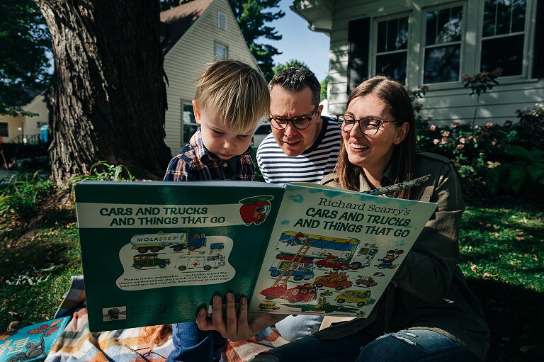 Family of three reads a book on the front lawn