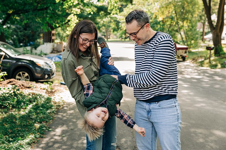 Mom holds toddler upside down while dad tickles son an everyone smiles 