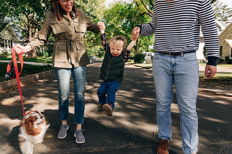 family of three goes for a walk and swings toddler son