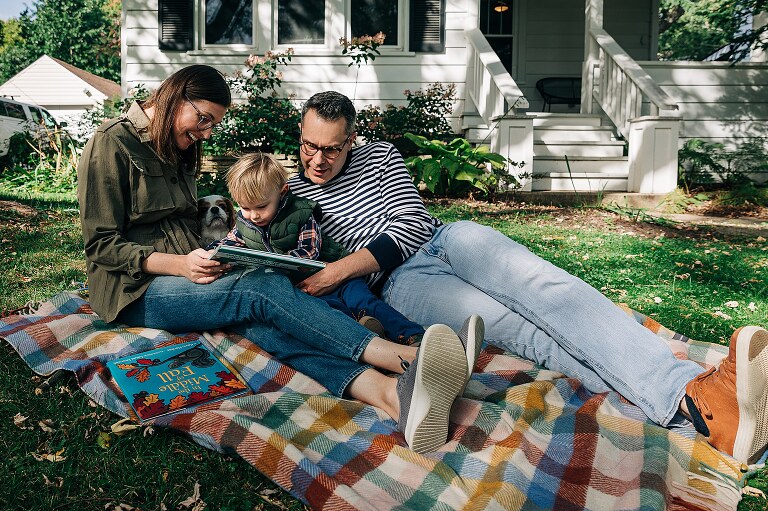 Family of three sit on front lawn reading books 