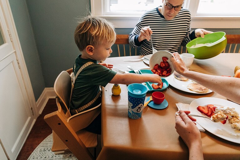 mom gives son more strawberries on his plate for Saturday pancakes 