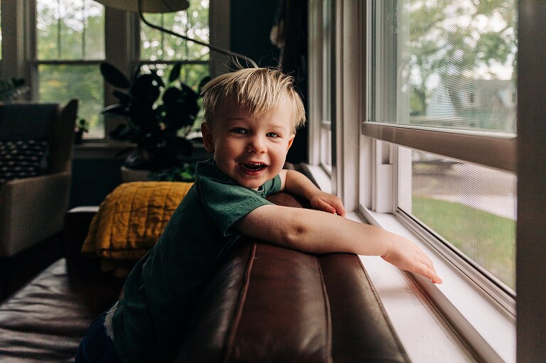 Smiling toddler sits on couch, camera aware