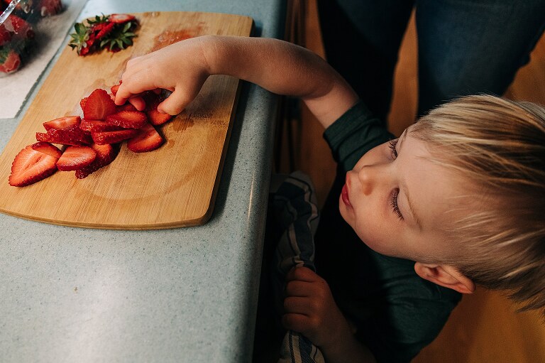 toddler boy reaches for sliced strawberries