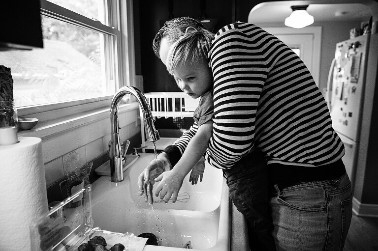 black and white. dad helps toddler son wash his hands before Saturday pancakes 