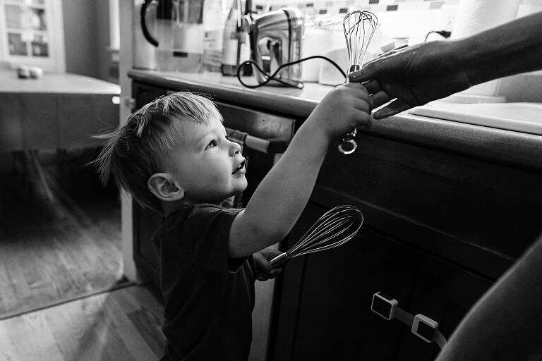 black and white. Mom hands toddler a whisk beater of whipped cream in the kitchen 