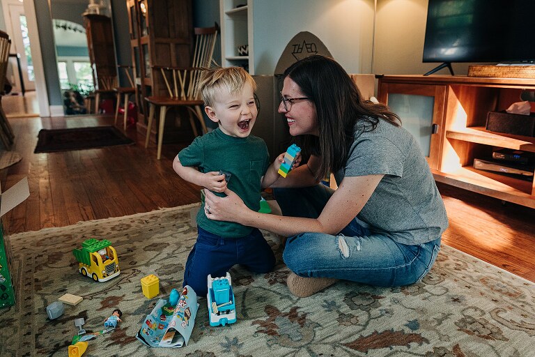 mom tickles toddler son while playing in the living room, both are smiling 