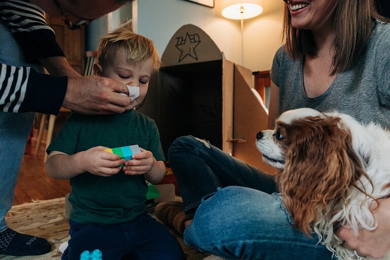dad wipes son's nose while dog looks on and mom smiles 