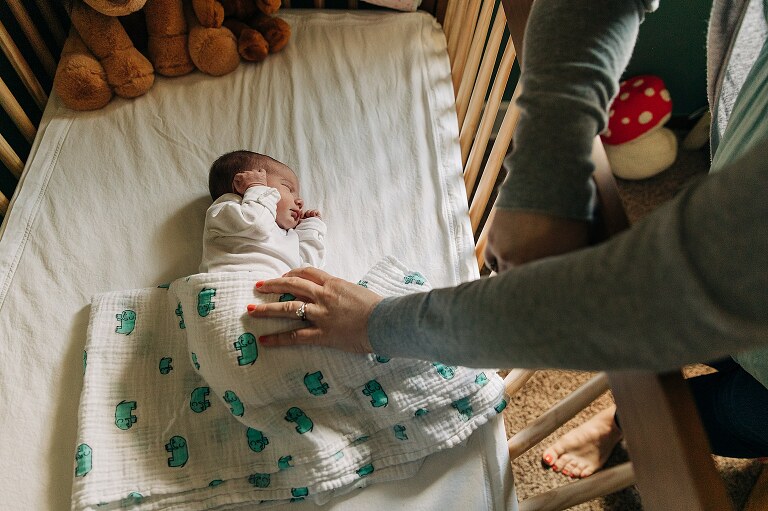 mom reaches hand in crib to touch sleeping newborn 