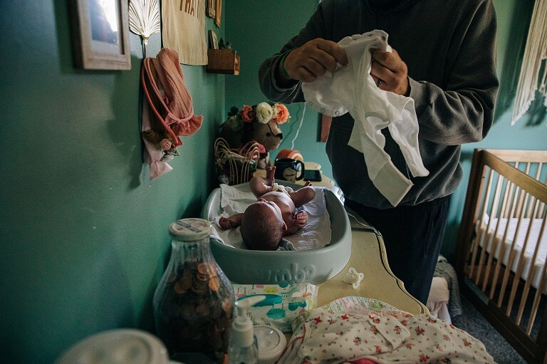 dad puts onesie on a newborn who is on changing pad on a quiet summer morning