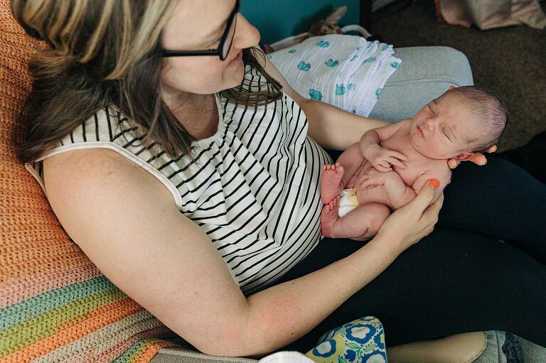 top down view of mom holding newborn in her lap, subtle window light illuminating them
