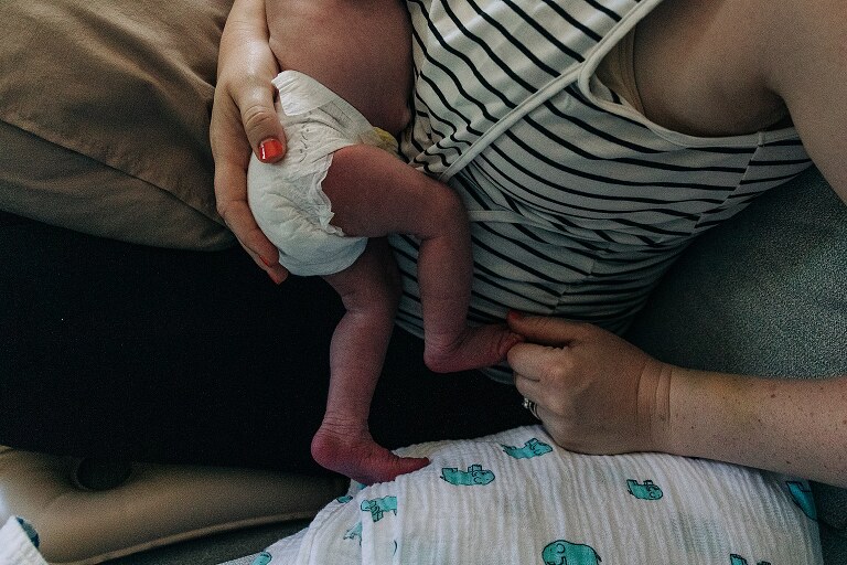 details of mom holding newborn feet while nursing