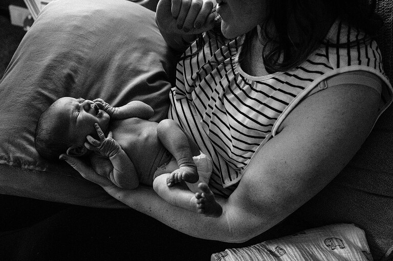 black and white of newborn in subtle window light being held by mother on a quiet summer morning