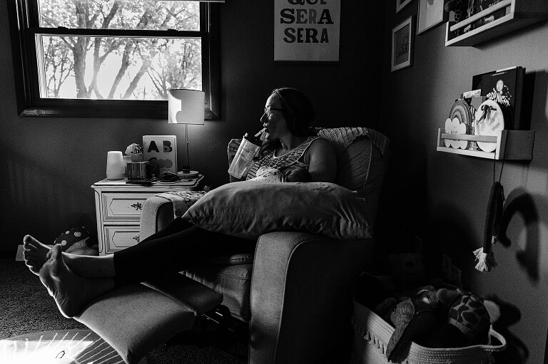 black and white. Mom drinks from the hospital water jug while nursing newborn on a quiet summer morning