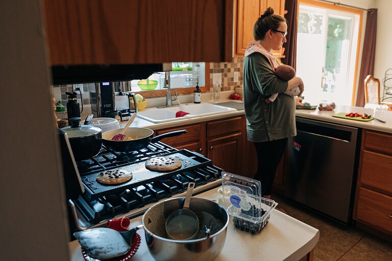 mom holds newborn while pancakes cook on the griddle 