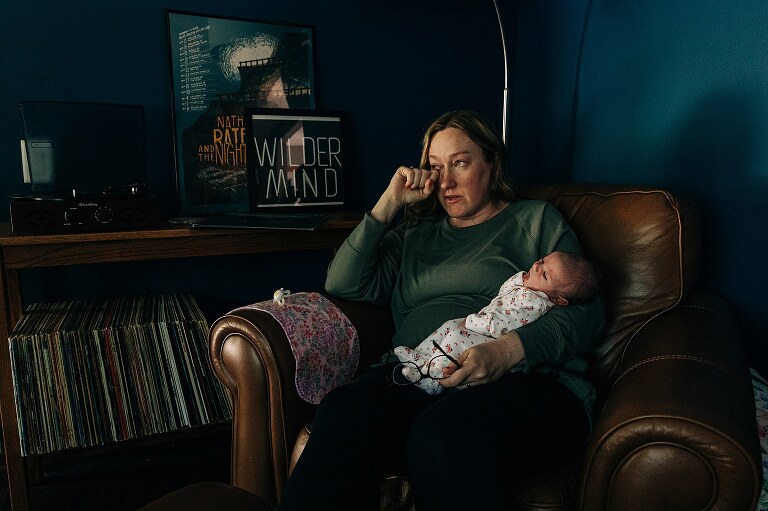 new mom wipes away a tear while holding newborn on a quiet summer morning