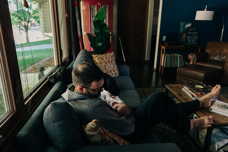 Dad holds newborn on couch in window light