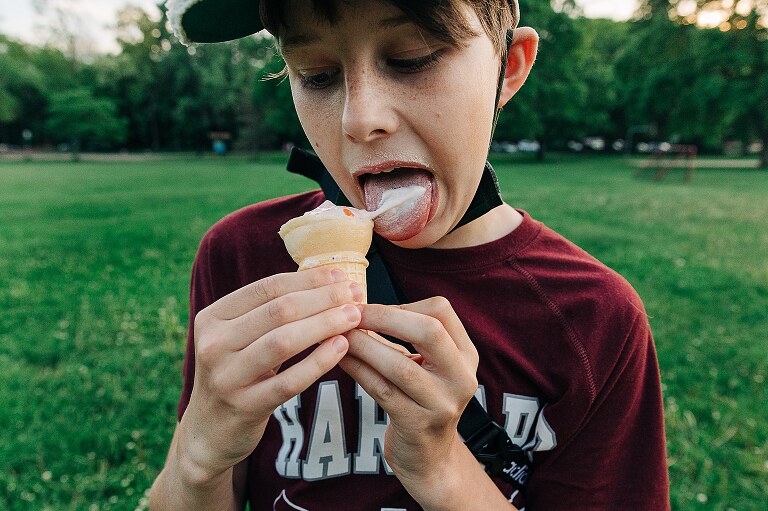 boy wearing a baseball hat licks ice cream cone in a park