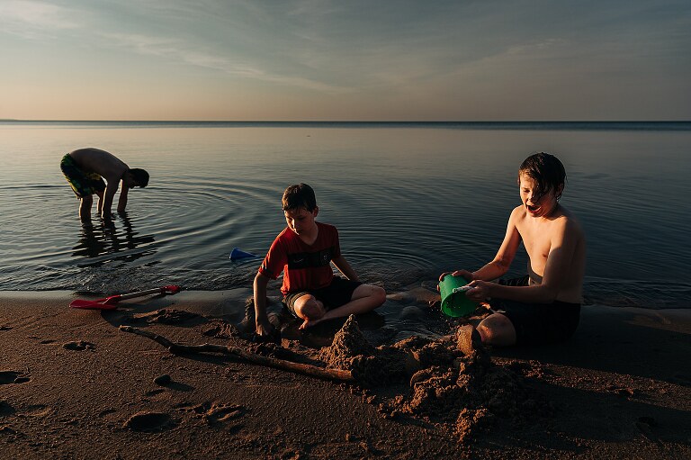 Three boys play on the beach at sunset 