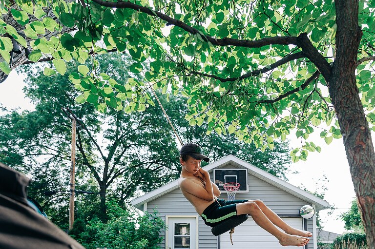 boy swings from a tire swing in a backyard on a summer's day