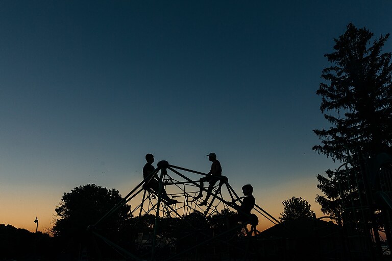 three kids are sitting on a play structure and silhouetted against twilight sky