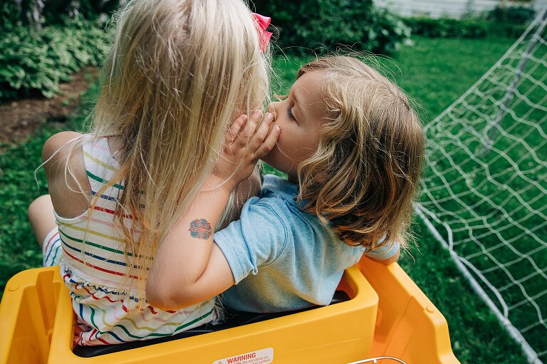 small child cups hand and whispers in ear of older child while riding on a toy car on summer nights 