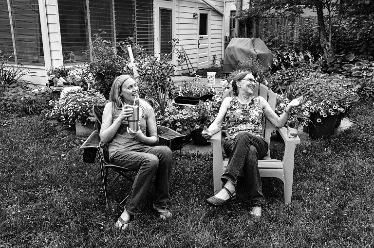 b/w adult daughter and mother sit on chairs in the backyard and laugh