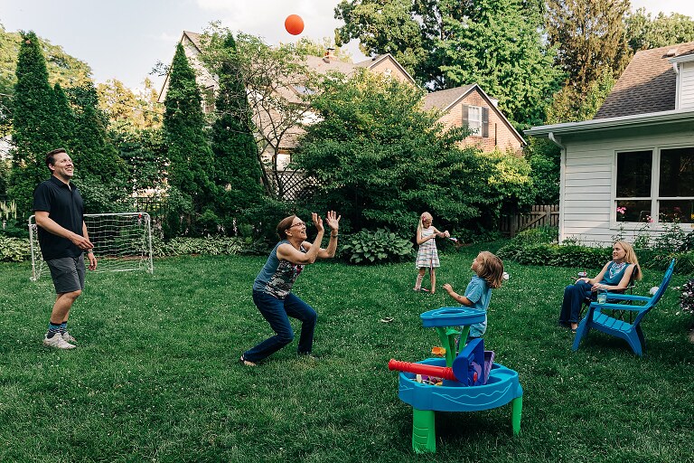 Grandma plays Keep Away game in the backyard with grandchildren and grownups. a red ball is in the air. Summer nights