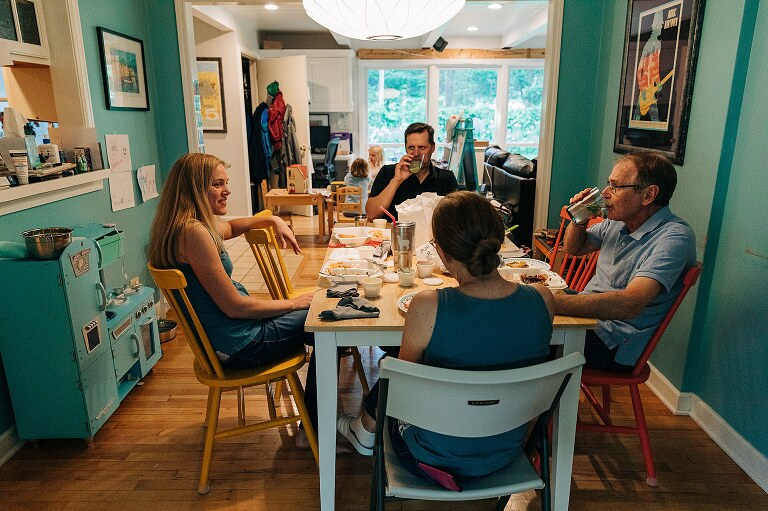 Parents and grandparents linger at the table together while kids are visibly playing in next room over on summer nights